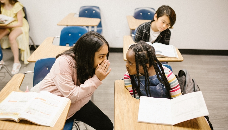 Two people gossiping about a classmate.